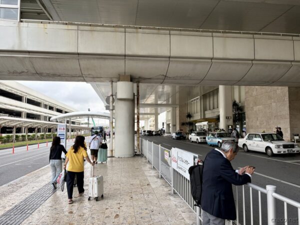 那覇空港到着ターミナルの高架下歩道。スーツケースを引く観光客と並ぶタクシー乗り場、沖縄旅行初日の到着時の光景。