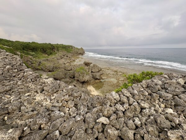 具志川城跡の石垣越しに見下ろす磯浜。ゴツゴツした隆起珊瑚の岩場と小さな砂浜、南部ドライブで訪れた海岸景観。