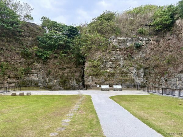 南城市・港川遺跡公園の断崖の谷底の広場。琉球石灰岩の高い岩壁に囲まれた芝地と小径、朝の静かな遺跡公園の風景。