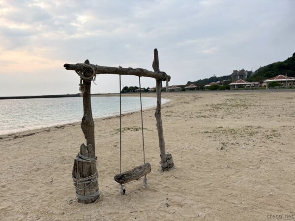 あざまサンサンビーチの流木ブランコを別角度から。奥に防波堤と沖合のコマカ島、南城市知念半島の朝の静寂。