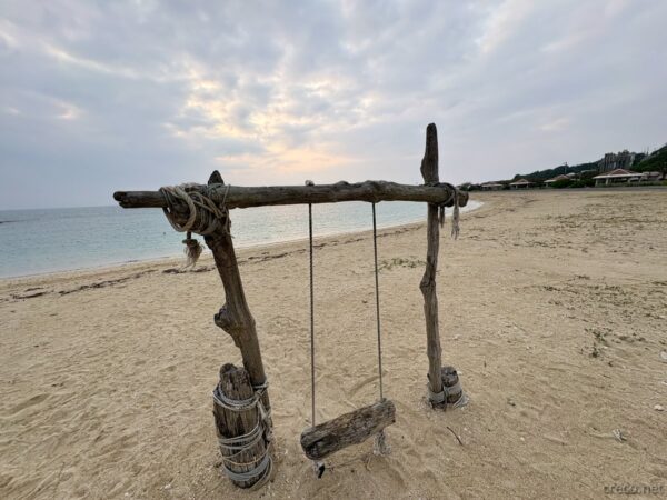 あざまサンサンビーチのブランコ越しに見る水平線。朝の淡い空と穏やかな海、旅の気分を盛り上げる人気撮影スポット。