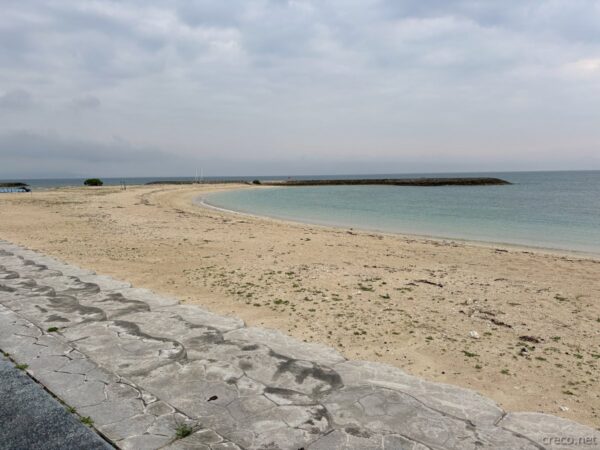 あざまサンサンビーチから望むコマカ島と渡し船乗り場。弓なりのビーチとターコイズブルーの入江、南城市あざまの桟橋と船。