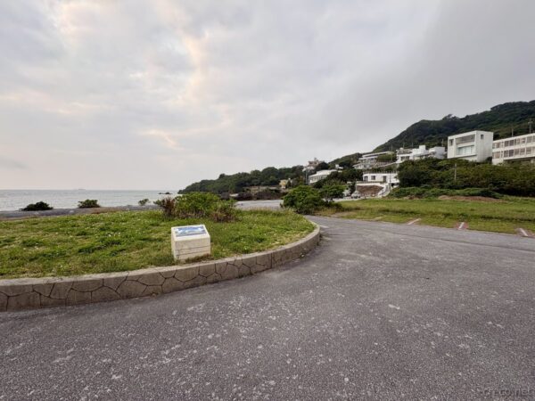 あざまサンサンビーチ案内板越しに見下ろす海岸線。海辺の集落と岬、知念半島の朝の俯瞰景観。