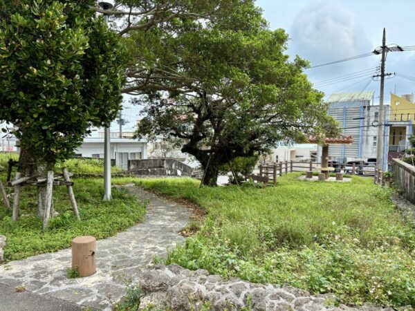 宮城島・具志川番所跡公園の入口。大きなガジュマルの木と琉球石灰岩の石積み、背後に瓦屋根の東屋が見える集落の史跡公園。