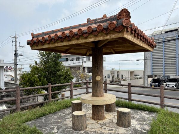 宮城島・具志川番所跡公園の赤瓦屋根の東屋。シーサー瓦と木製の丸太椅子が並ぶ、沖ツラ聖地の撮影ポイント。