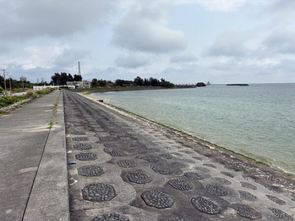 具志川ビーチの護岸遊歩道の長大な眺め。ずっと続く六角ブロックと青い海、奥に宮城島のリゾートホテルが霞む海岸線。
