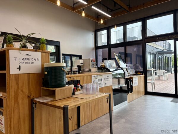 やんばるパイナップルの丘 安波の店内カウンター。返却口と観光パンフレット、ガラス越しに見える緑豊かなやんばるの風景。