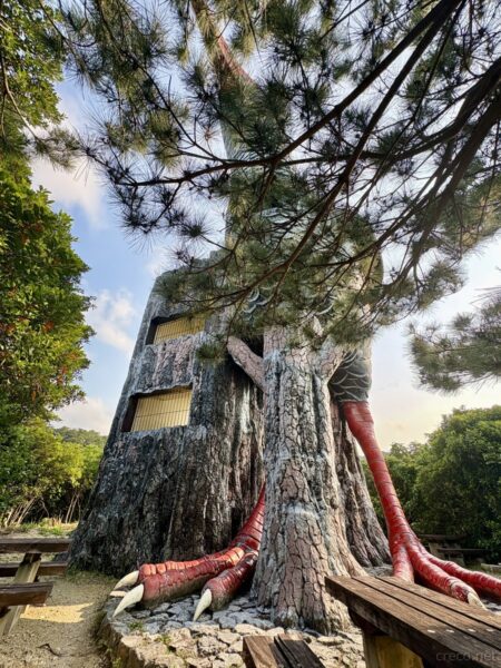 辺戸岬のヤンバルクイナ展望台を見上げる。木肌に紛れるカムフラージュ柄の巨大塔、沖縄北端のシンボルモニュメント。