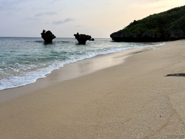 ティーヌ浜のハートロックと白波の打ち寄せる砂浜。古宇利島北側の静かな朝、恋愛成就のスポットで有名な岩。