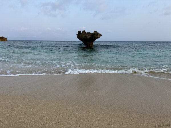 ハートロックを砂浜の波打ち際から見上げる。朝の柔らかい光に照らされる古宇利島ティーヌ浜のシンボル。