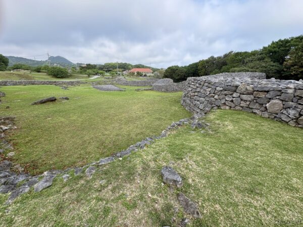 今帰仁城跡の内郭遺構。草地と散在する石造建物跡、奥に赤瓦の民家、世界遺産グスクの開けた曲輪。