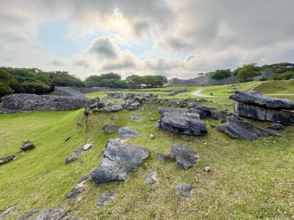 今帰仁城跡の大庭（ウーミャ）。芝の広場に散らばる石と石灰岩の塊、奥に城壁が続く世界遺産の中心部。