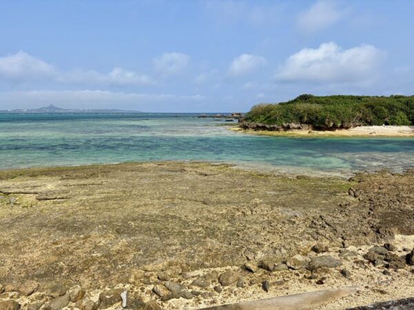備瀬崎から望む伊江島とエメラルドブルーの海。潮が引いて露出した岩礁の礁原、沖縄本島北部の絶景海岸。