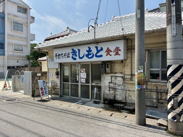 本部町の名店「きしもと食堂」外観。赤瓦屋根と大きな青い看板「手打ちそば きしもと食堂」、沖縄そば発祥の老舗。