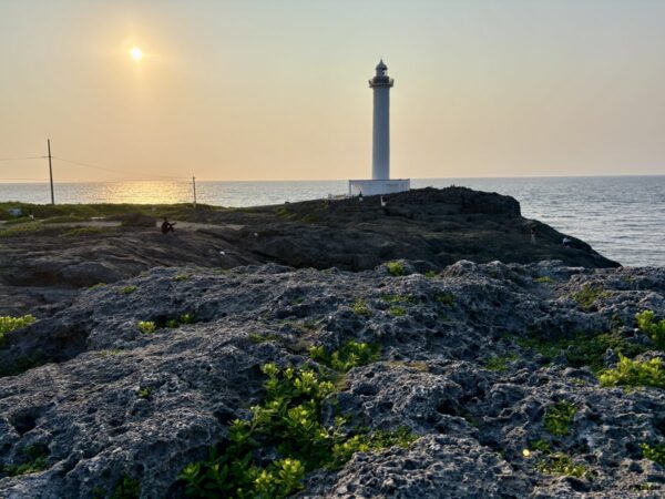 残波岬の夕景と灯台シルエット。岩礁に夕日が映り、白い灯台がシンメトリーに並ぶ読谷村の定番絶景。