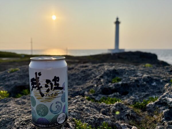 残波岬の夕日と残波ハイボール缶。岩の上に置いた泡盛ハイボール缶越しに灯台と夕陽、沖縄の絶景に乾杯。