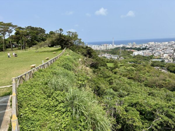 浦添城跡の崖縁に広がる芝生の見晴台。遠くに那覇の高層ビル群と東シナ海、見晴らしの良い丘上の展望。