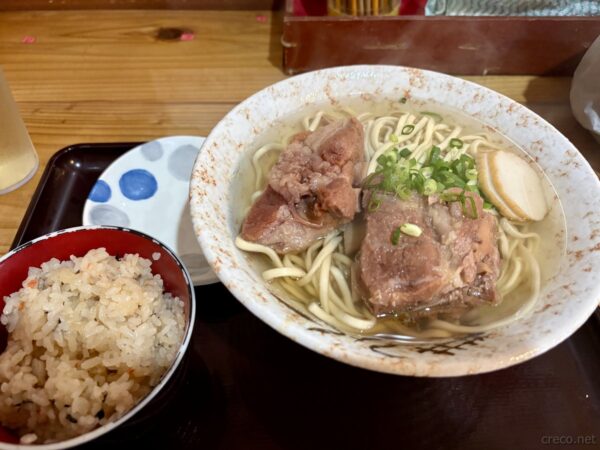 那覇の食堂の沖縄そばとジューシーセット。太麺にソーキ、ネギ、カマボコ、炊き込みご飯のジューシー小鉢、沖縄のソウルフード。