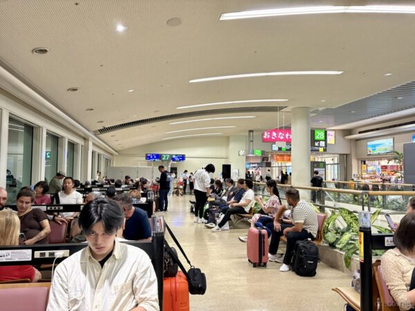 那覇空港国内線ターミナル夜の搭乗待合室。27・28番ゲート案内板と待機する乗客たち、本土帰還直前の沖縄空港の光景。