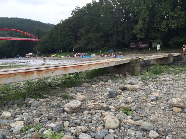 飯能河原の夏の賑わい、奥に赤い割岩橋と河川敷で遊ぶ人々