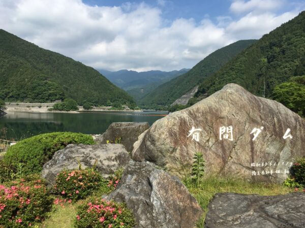 有間ダムの石碑と湖、緑の山々に囲まれた青い湖面と空