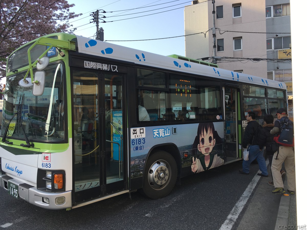 東飯能駅前を走行する国際興業バス、青いラッピングに天覧山とここながデザインされたヤマノススメラッピングバス