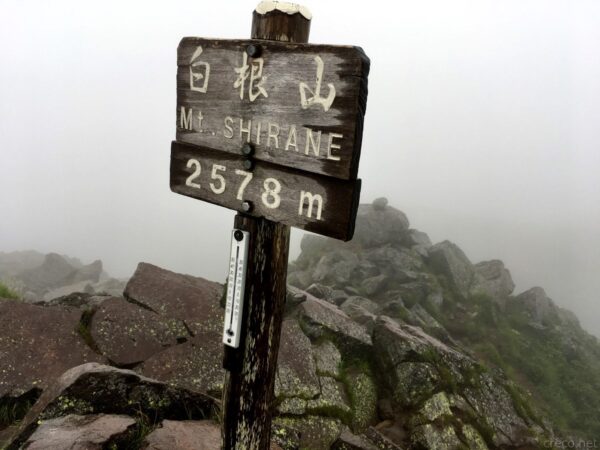 日光白根山山頂、「白根山 Mt.SHIRANE 2578m」の木製山頂標識と温度計、濃霧に包まれた苔むす岩稜帯