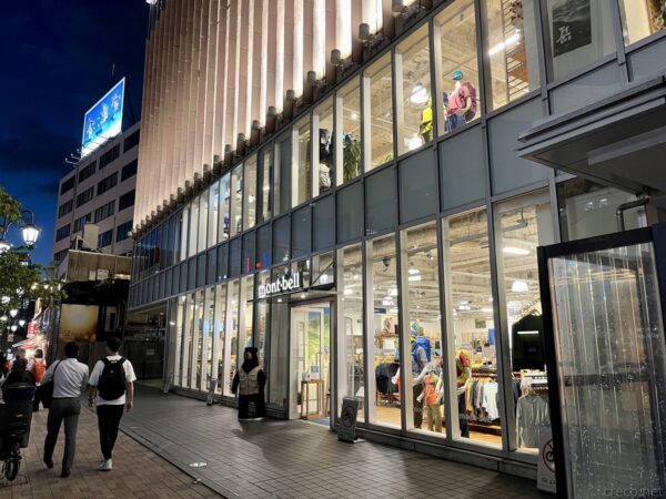 夜のモンベル恵比寿店外観、ガラス張りの2階建て店舗が暖色照明で明るく照らされ、入口横に黒クマのマスコットが立つ(2023年8月14日閉店)