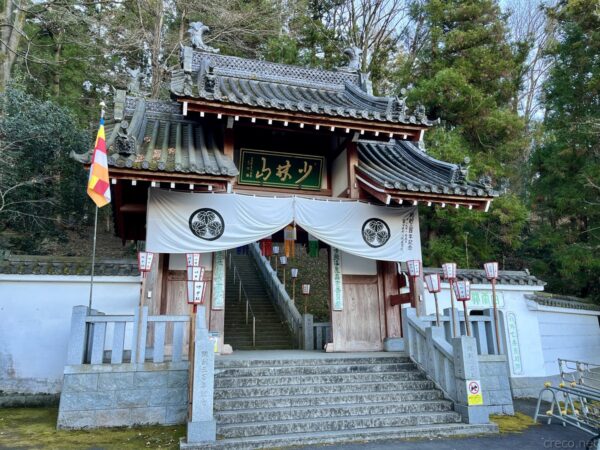 群馬県高崎市・少林山達磨寺の総門、瓦屋根に「少林山」の緑扁額、白い幕に三つ葉葵の家紋、両脇に赤い奉納提灯