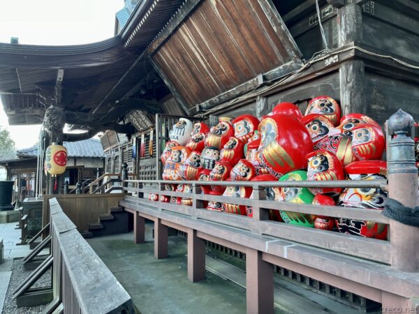 少林山達磨寺の本堂縁側、奉納された大量の赤い高崎だるまが山積み、左に「達磨寺」の赤提灯