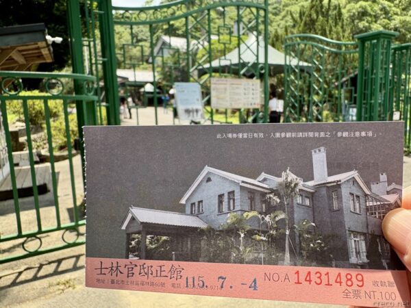 手にした士林官邸正館の入場券。洋館の写真と「士林官邸正館 全票 NT.100」の印字、日付115.7.-4があり、背後に緑の門。