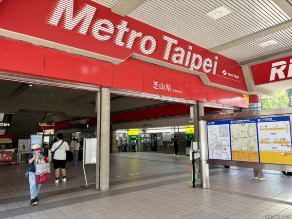 台北メトロ芝山站(Zhishan)の駅入口。赤い「Metro Taipei」の大看板の下に改札とサインが並び、路線図の前を人が歩く。
