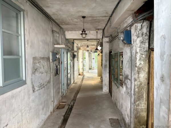寶藏巖の古い建物の内部通路。剥がれた漆喰の壁が続く薄暗い廊下に古い照明が下がり、奥の出口から光が差し込む。