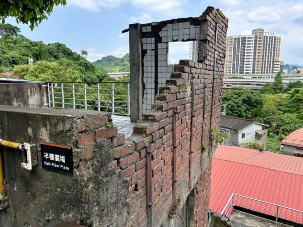 寶藏巖の「半樓廣場 Half-Floor Plaza」。窓枠だけを残した崩れかけの煉瓦壁が保存され、背後に緑の丘と高層ビルが見える。
