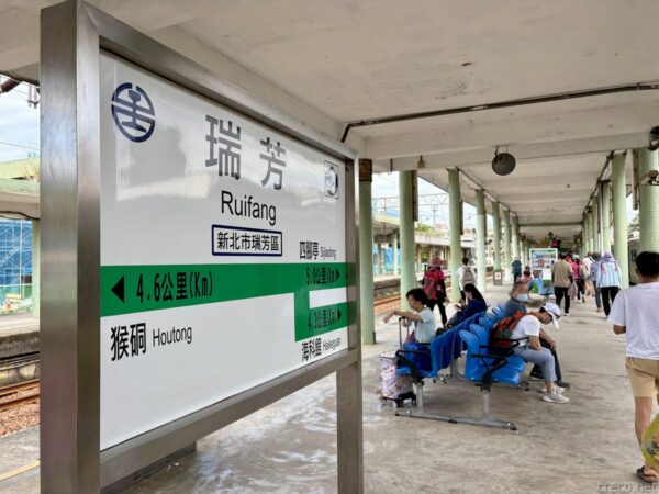 瑞芳（Ruifang）駅ホームの緑白の駅名標。猴硐・四脚亭方面の案内が中国語で記され、屋根の下の青いベンチに乗客が座って列車を待つ。