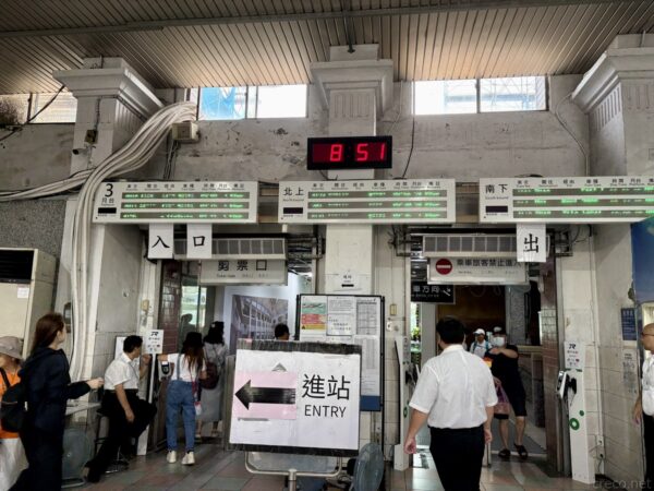 瑞芳駅の改札口。「入口 剪票口」「出口」の看板が並び、電光時計は8時51分。「進站 ENTRY」の矢印看板の脇を制服の駅員や乗客が行き交う。