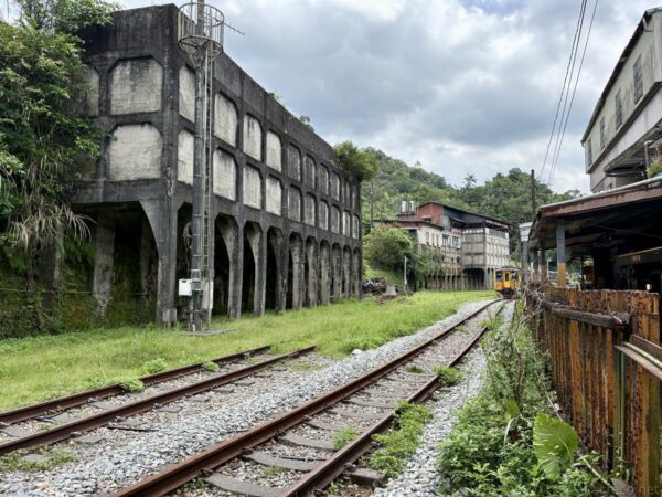 菁桐駅付近の線路と旧選炭場。手前で三本の線路が分岐し、左手にコンクリート造アーチが連なる旧選炭場の巨大な遺構、右手に駅舎の屋根と山の緑が広がる。