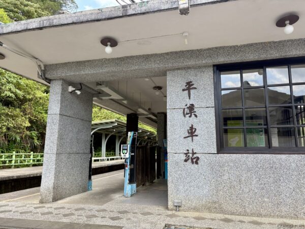 「平溪車站」と縦書きで刻まれた石造の駅舎入口。灰色の御影石の柱と黒枠の窓、緑に囲まれた落ち着いたたたずまいの駅。