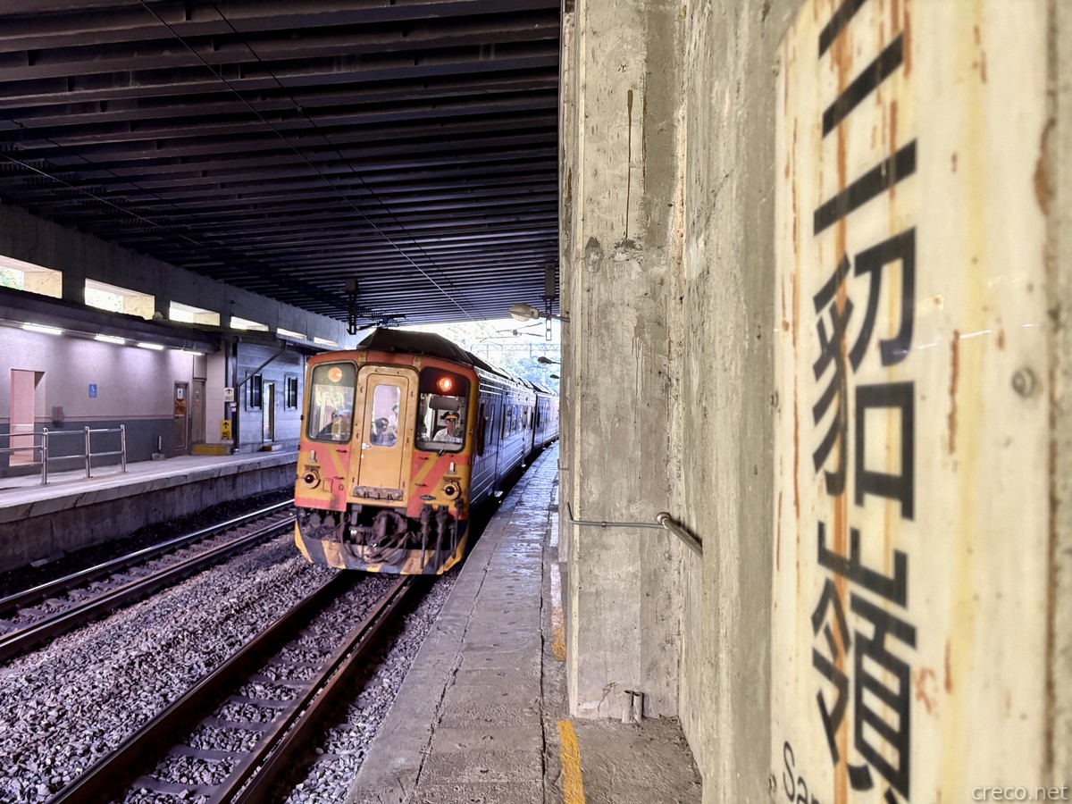 三貂嶺駅の薄暗いホームに停車する橙の旧型列車。右手のコンクリート柱に「三貂嶺」と大書され、複線の線路が奥へ延びる。