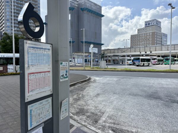 前橋駅ロータリー脇のバス停ポール6番。時刻表の掲示があり、正面に東横インやペデストリアンデッキ、複数の路線バスが並ぶ駅前広場。朝の薄曇りの空。