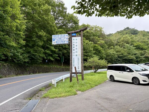 荒山高原登山口の県道脇に立つ道標。「あかぎ木の家」「荒山高原登山口」「赤城森林公園」と記した青い案内板と木製標柱、ガードレール、駐車した白いワゴン車。
