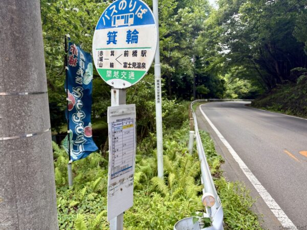 帰りに立ち寄った「箕輪」バス停の丸い標識。赤城山・前橋駅・富士見温泉方面を示し、やきとうもろこしののぼりと時刻表、カーブする県道とガードレール。